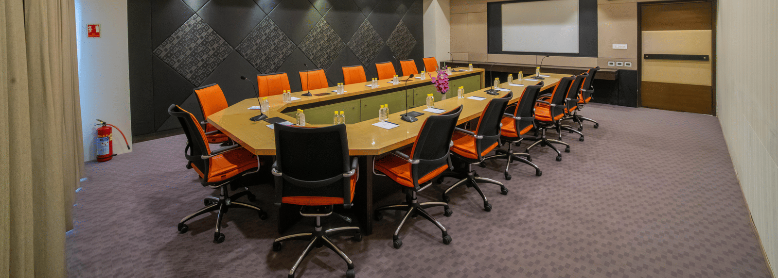 Conference room with a long table, orange chairs, and presentation screen at Narayani Heights Hotel & Resorts, Ahmedabad.