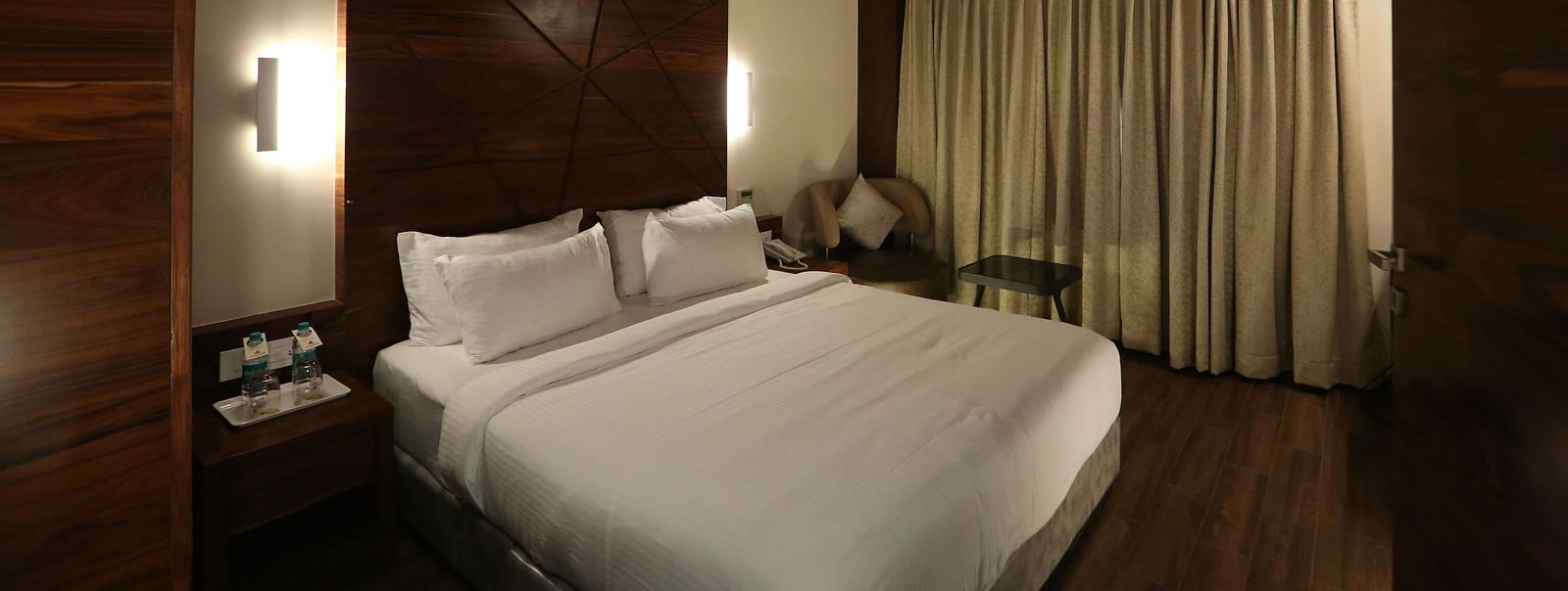 Premium Suite featuring a king size bed, bedside tables, lamps, and dark wood panelling - TGI SPS Grand, Coimbatore