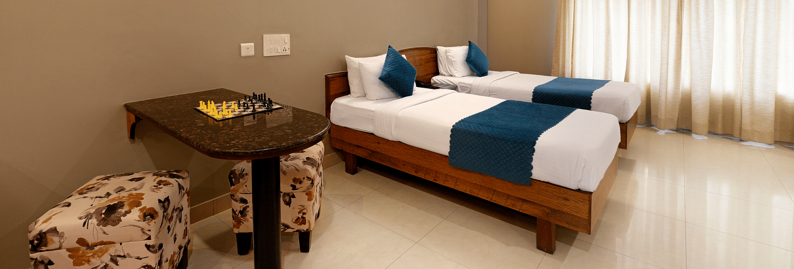 A Deluxe Room with a desk, twin beds, and bright natural light coming from the window - Cross Roads Inn, Bengaluru
