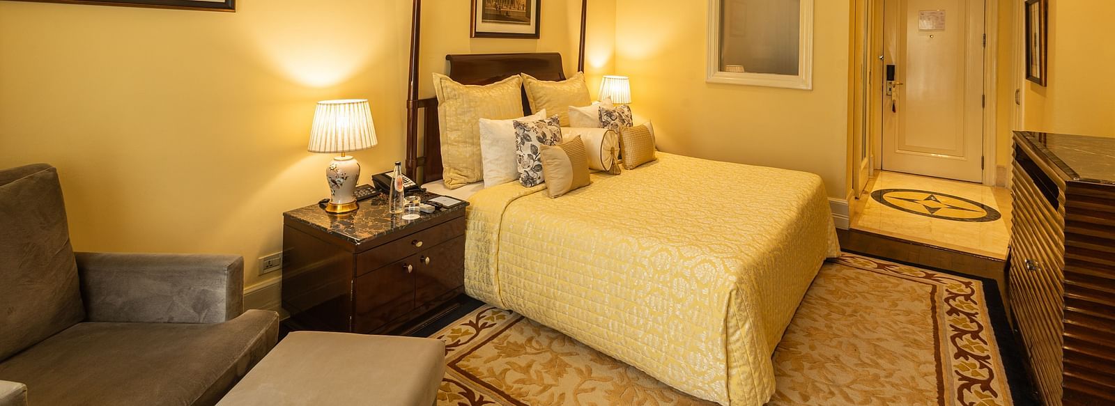 Side view of the Deluxe King Bed Room Pool View at The Claridges New Delhi, featuring a cosy king sized bed, wall-mounted TV, and bedside lamps
