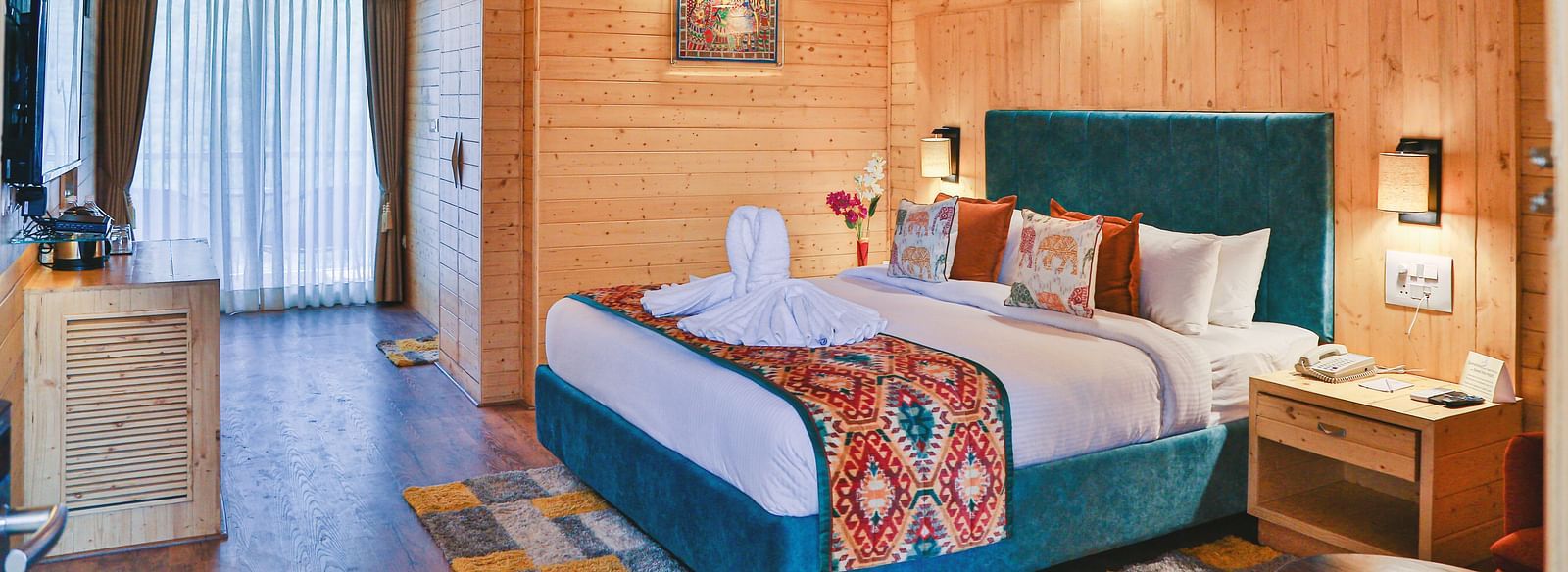 A cosy bedroom with wooden paneling, a table, curtains, a plush bed and warm lighting. - Bamboo Saa Resort & Spa, Udaipur