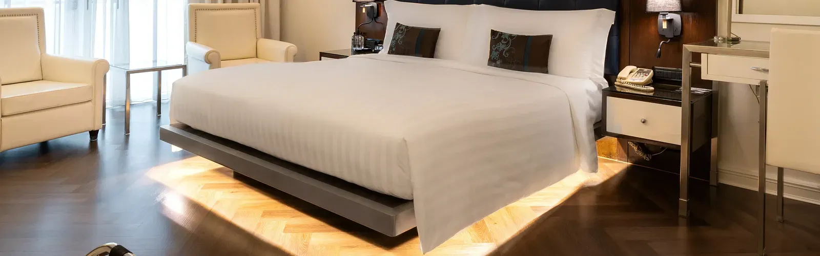 Luxury suite with platform bed, under-bed lighting, and lounge chair at Night Hotel Bangkok.