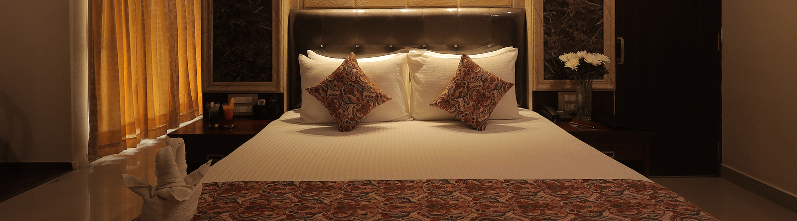 An image of a bedroom with bedside table, a set of table and chairs, flat TV screen, and AC - Sathyam Grand Resort