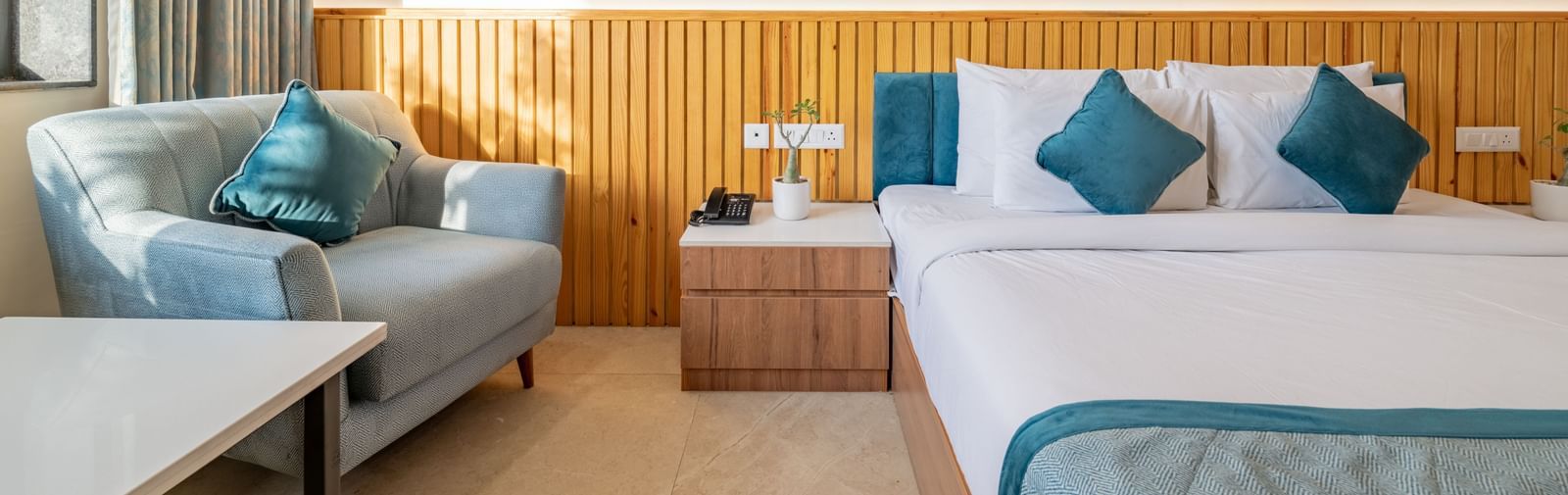 Guest room at Hotel Highway King, Bagru, featuring a double bed, armchair, bedside table, and a large window with curtains.