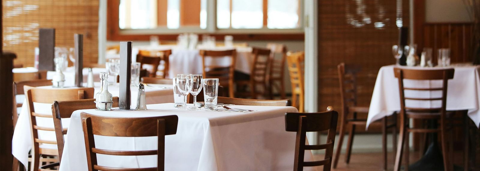 A dining room with wooden tables set with white tablecloths and chairs.