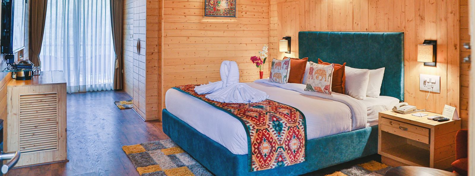 A cosy bedroom with wooden paneling, curtains, a plush bed and warm lighting. - Bamboo Saa Resort & Spa, Udaipur