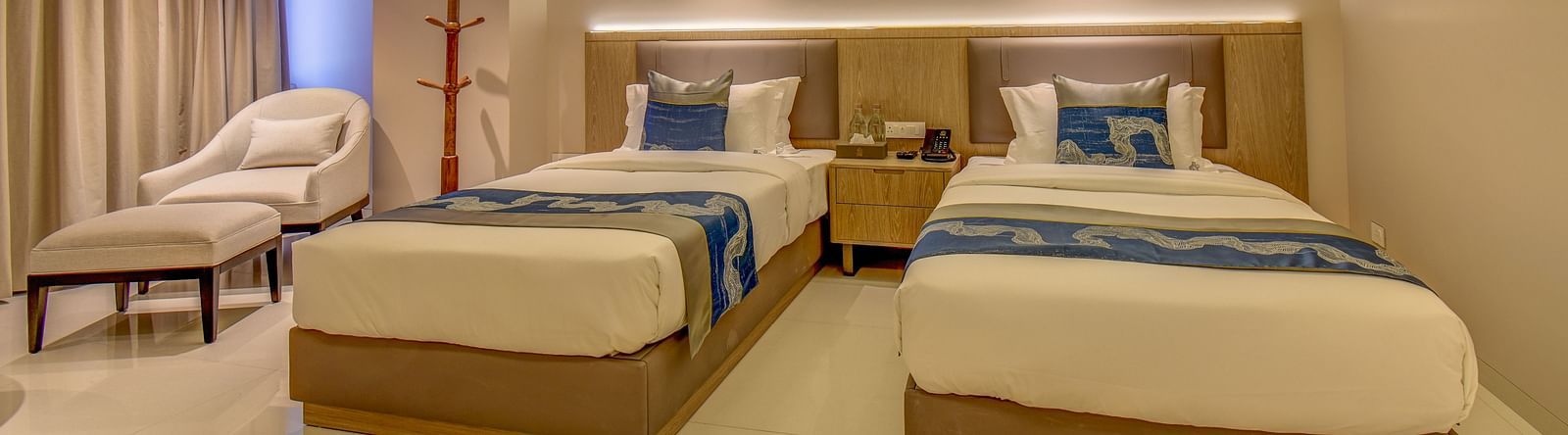 A well-lit Premium Twin room at The SSK Solitaire Boutique Hotel & Spa, Gangapur Road - Nashik featuring a twin  bed, two armchairs, a small table, and a work desk with a chair.