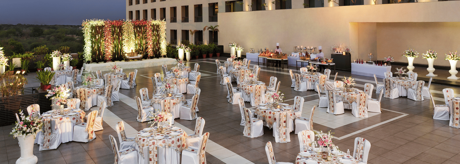 Outdoor banquet setup with white chairs and tables at Narayani Heights Hotel & Resorts, Ahmedabad.