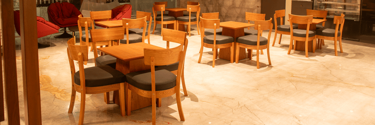 A hotel lobby area with wooden tables and chairs,  cushioned chairs, and ceiling lights arranged in a grid pattern.