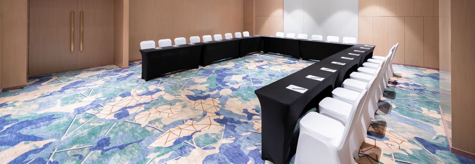 U-shaped boardroom setup with sleek chairs and patterned carpet at Merlis Hotel, Coimbatore.