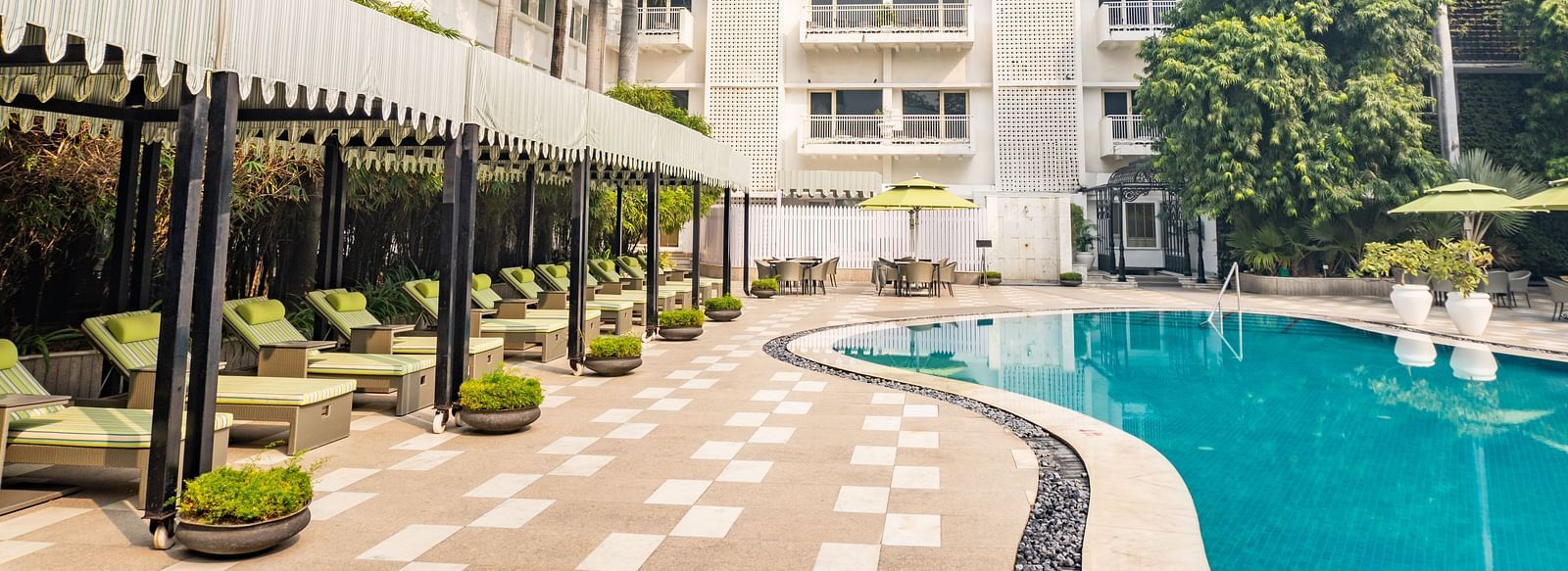 a bright facade image of The Claridges New Delhi with glittering blue swimming pool with green sunloungers