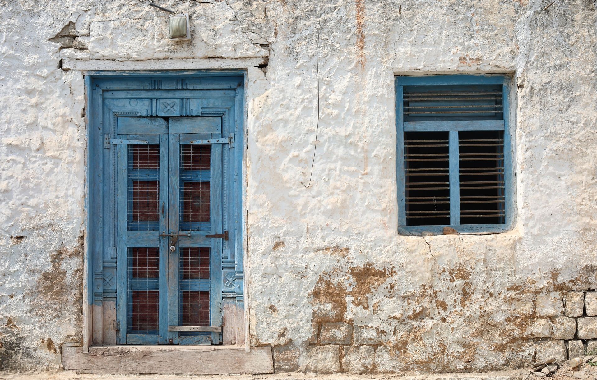 Old blue door and window on a weathered white wall.