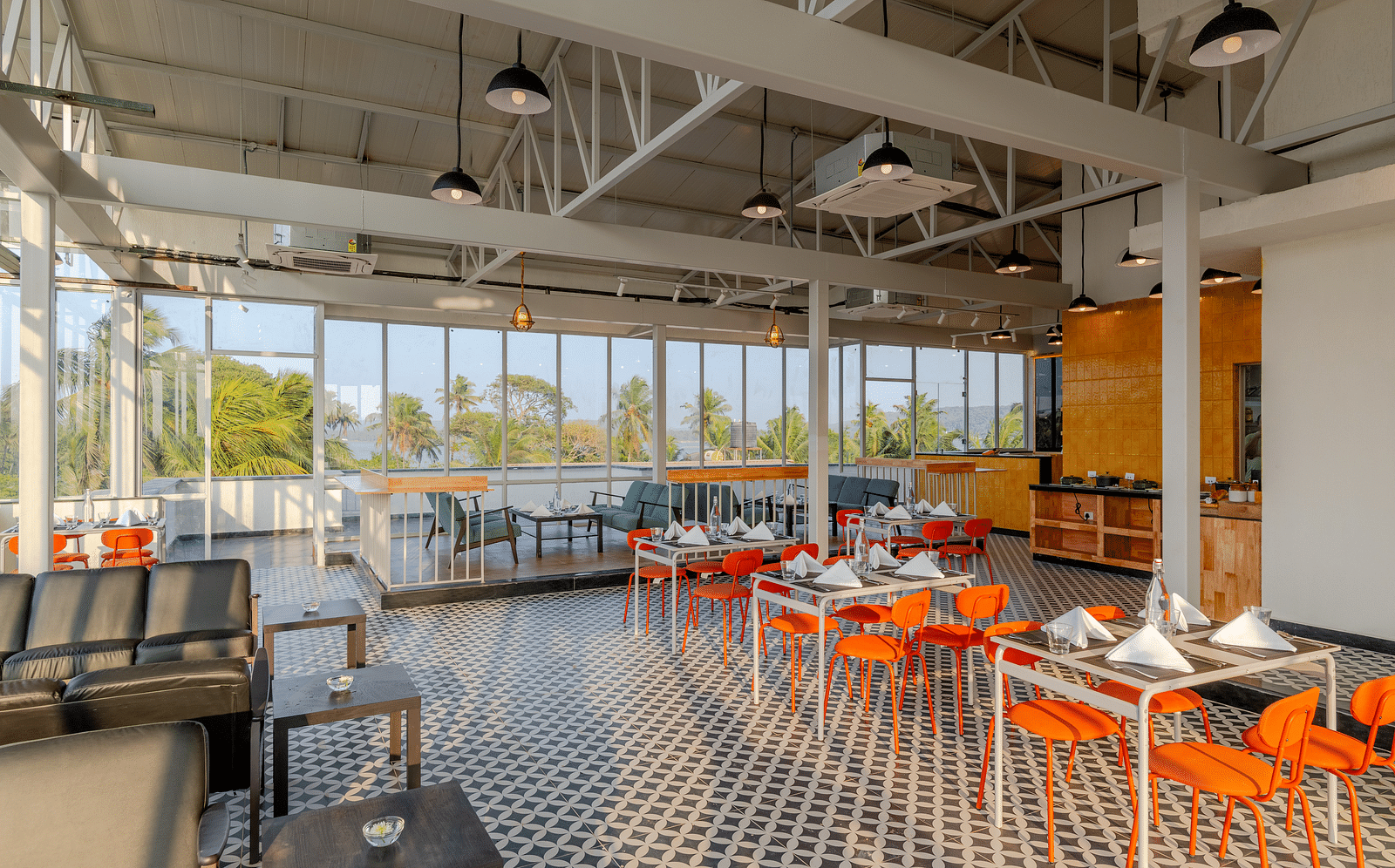  spacious and airy restaurant with industrial-style exposed ceiling, large windows letting in natural light, and a color palette of orange and grey, providing a relaxed dining atmosphere  at Bedzzz Xclusiv Morjim, Goa