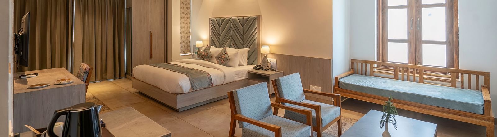 A spacious hotel room with a king size bed, a seating area, and a view of the lush green outdoors.