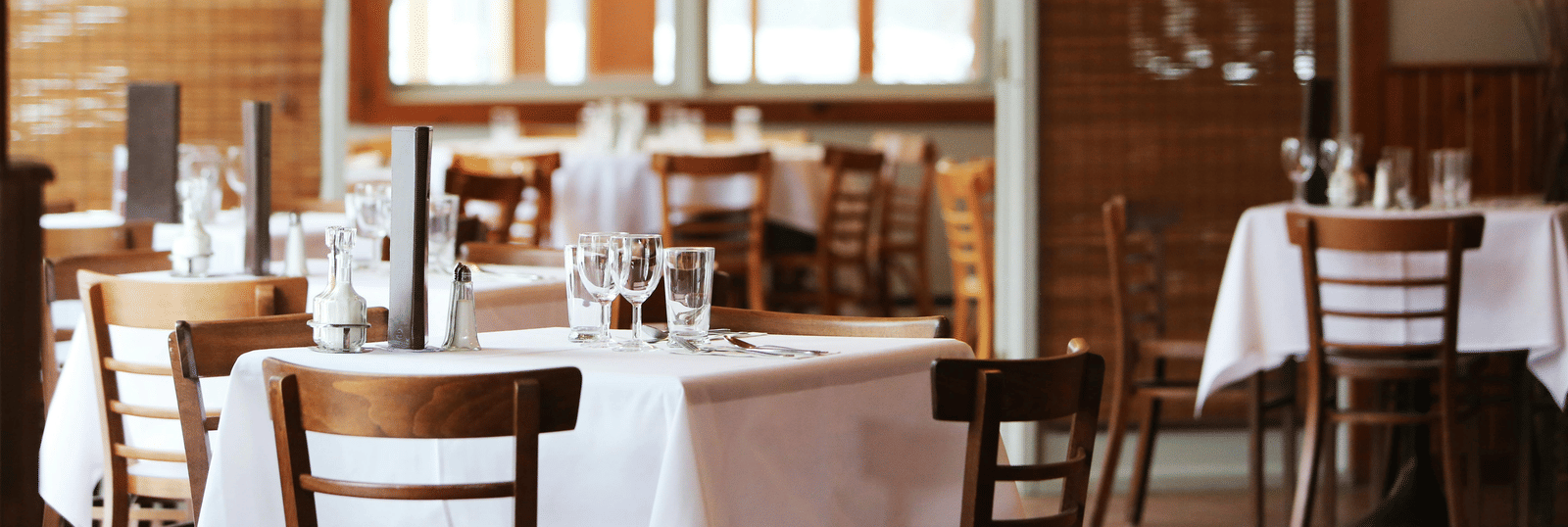 Elegant restaurant interior with neatly set tables, wooden chairs, and soft ambient lighting.