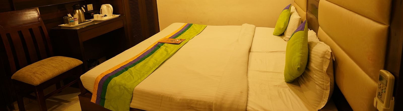 Standard Room furnished with a bed featuring white linens and green and yellow accents, two pillows, a chair, a desk, a television, and a wardrobe. - Hotel Dreamland, Chandigarh