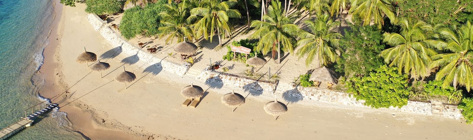 Aerial view of beach loungers and thatched umbrellas along shoreline at Flower Island Resort.