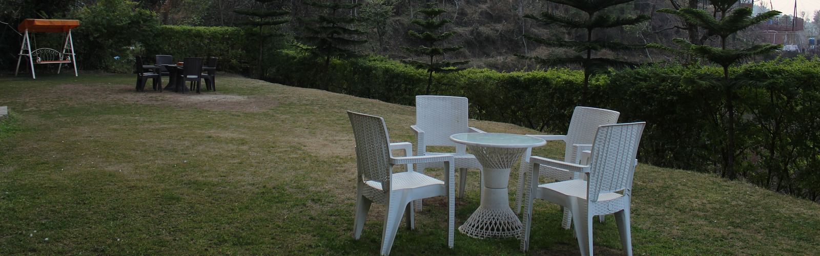 A beautifully maintained garden space with outdoor seating and a backdrop of hill slopes and trees at Dagshai Manor Kasauli - Inde Hotels.