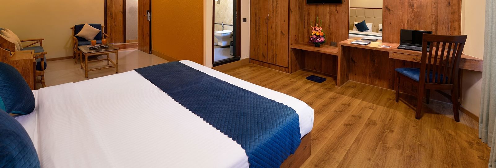 A well-furnished hotel room with a queen size bed, a seating area and wooden furniture - Cross Roads Inn, Bengaluru
