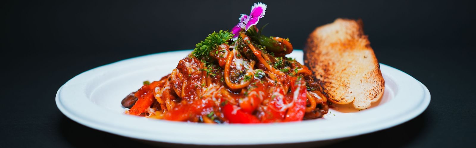 A gourmet pasta dish topped with rich tomato sauce, herbs, and an edible flower, served with a bread roll at D Café in Dip Holidays.