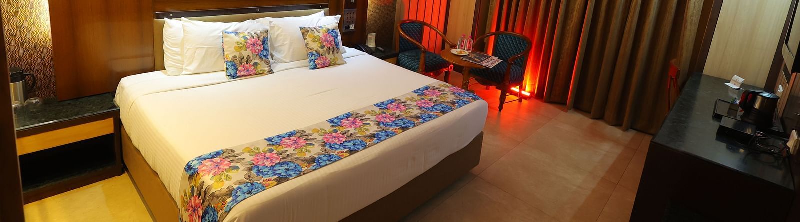  Overview image of a deluxe room at Hotel Amar with a bed, table, TV and huge window with curtains. 