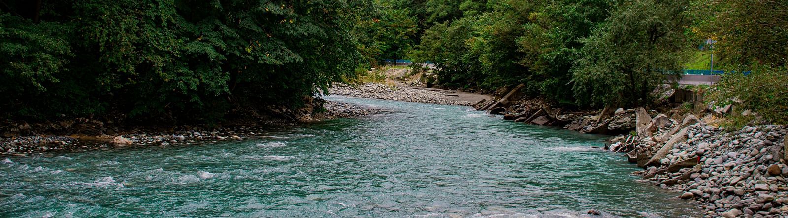 An overview of a river flowing in between rocks and trees on either side