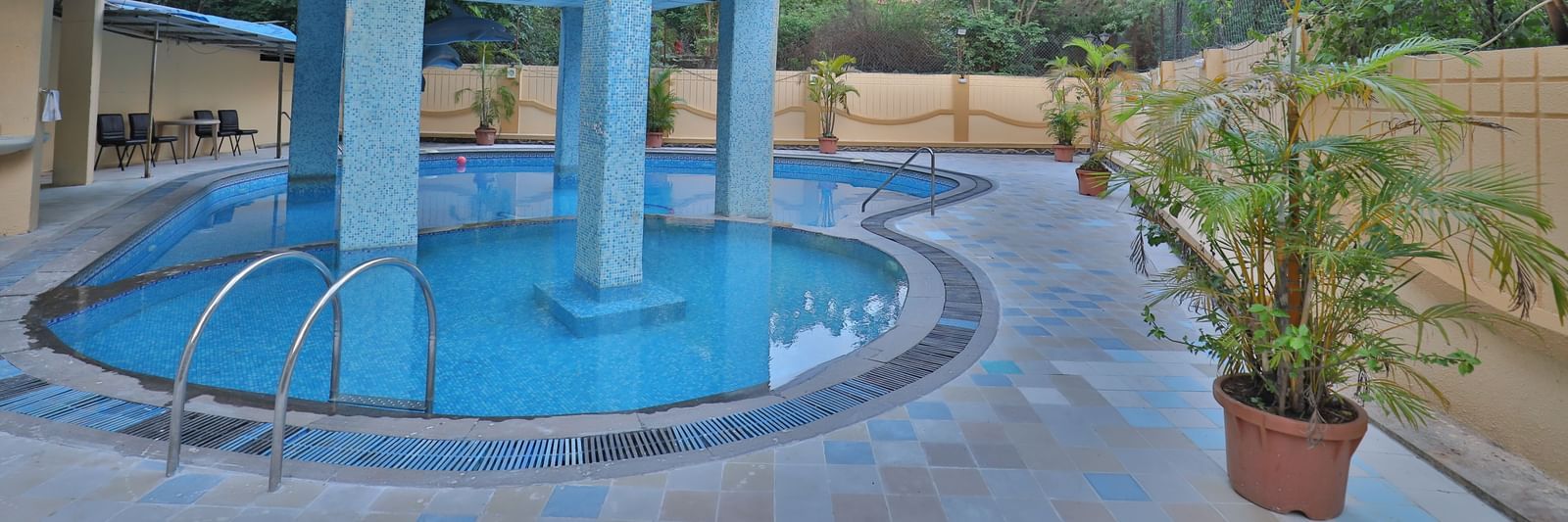 An outdoor swimming pool with blue water, surrounded by paved areas and the hotel building - Retreat Heritage, Lonavala