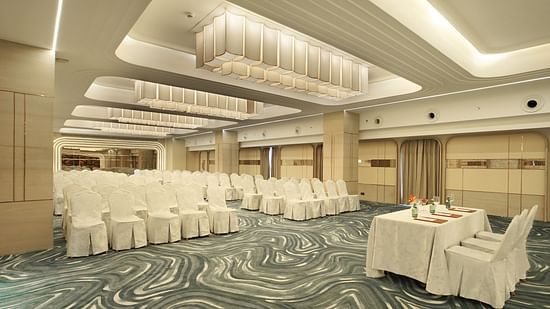 Conference room setup with numerous white chairs arranged in rows facing a white-draped table with floral centrepieces - The Orchid Hotel, Chandigarh