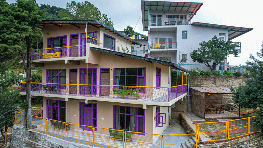 A multi storey building with balconies, railings, and surrounding greenery at Adrushya Estates, Mukteshwar.
