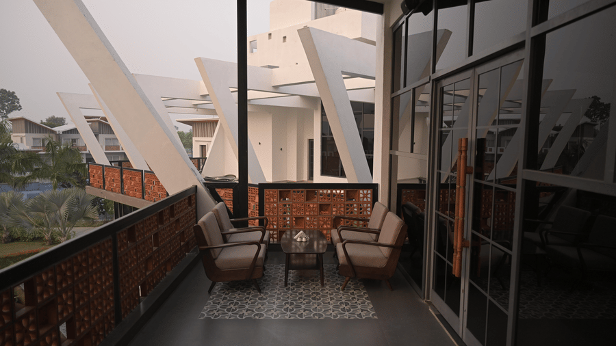 A cosy outdoor balcony with cushioned seating, brick accents, and modern architectural beams overlooking the greenery at Hotel Sonar Bangla Mayapur.