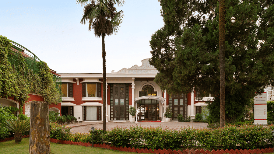 A 2-storey building structure, behind a lawn with palm trees and green plants at Ramada by Wyndham Mussoorie Mall Road.