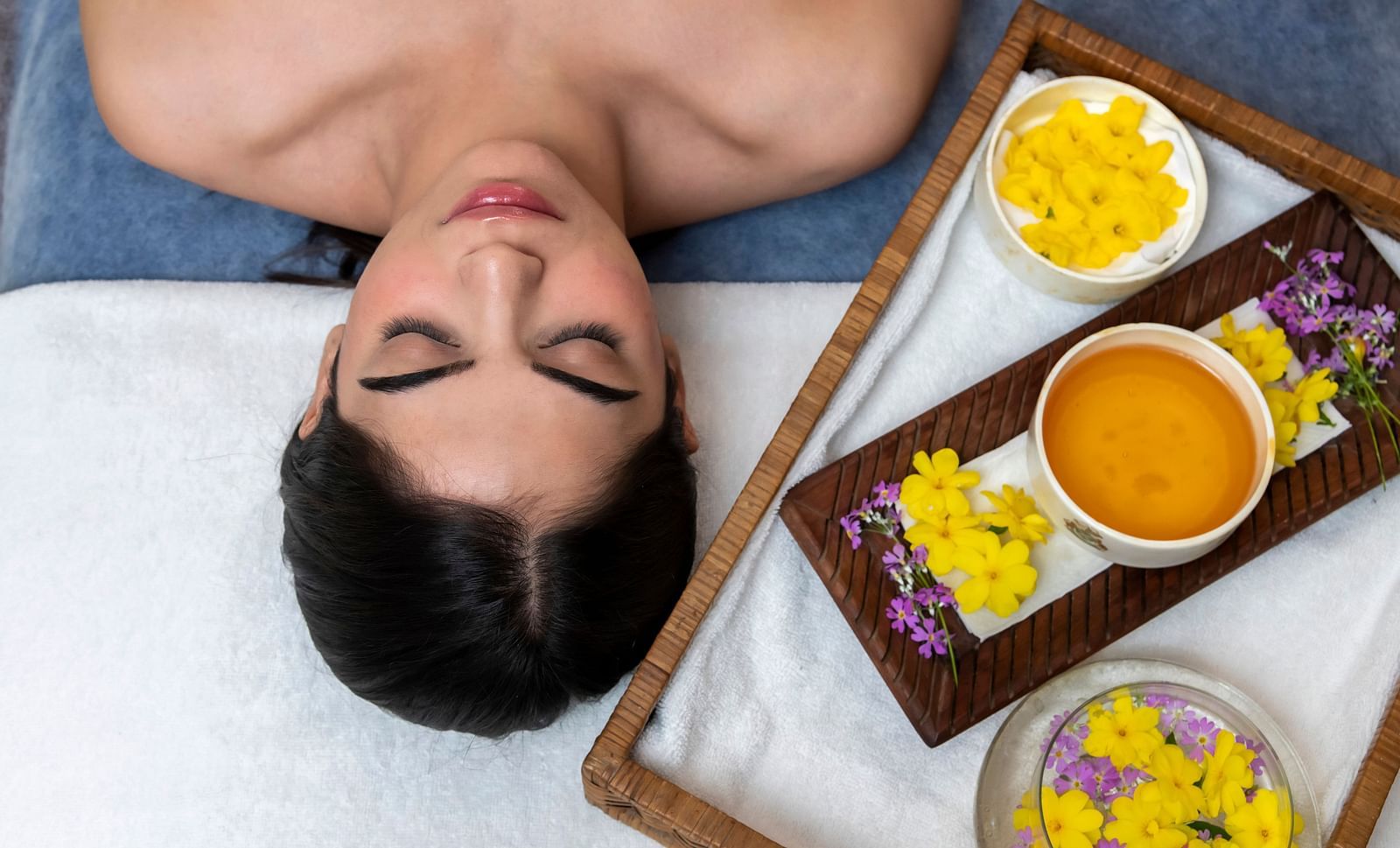 An image of a woman lying beside a tray of products used for spa treatments - Claridges Collection