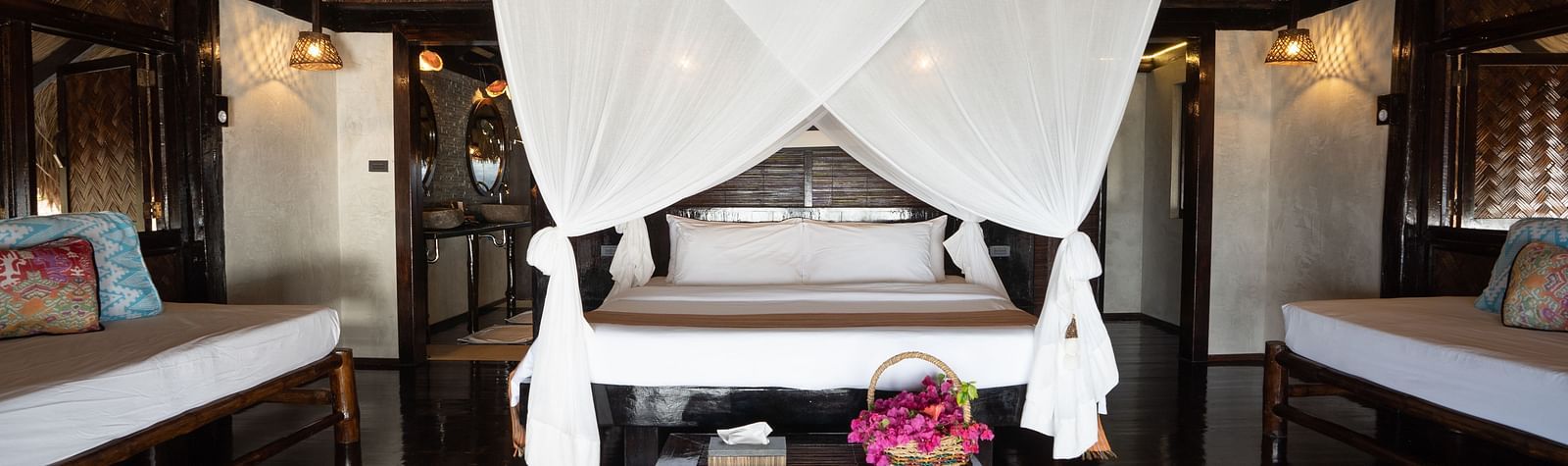 Wide-angle view of a canopy bed in a wooden room at Flower Island Resort and pink flowers placed on the bed.