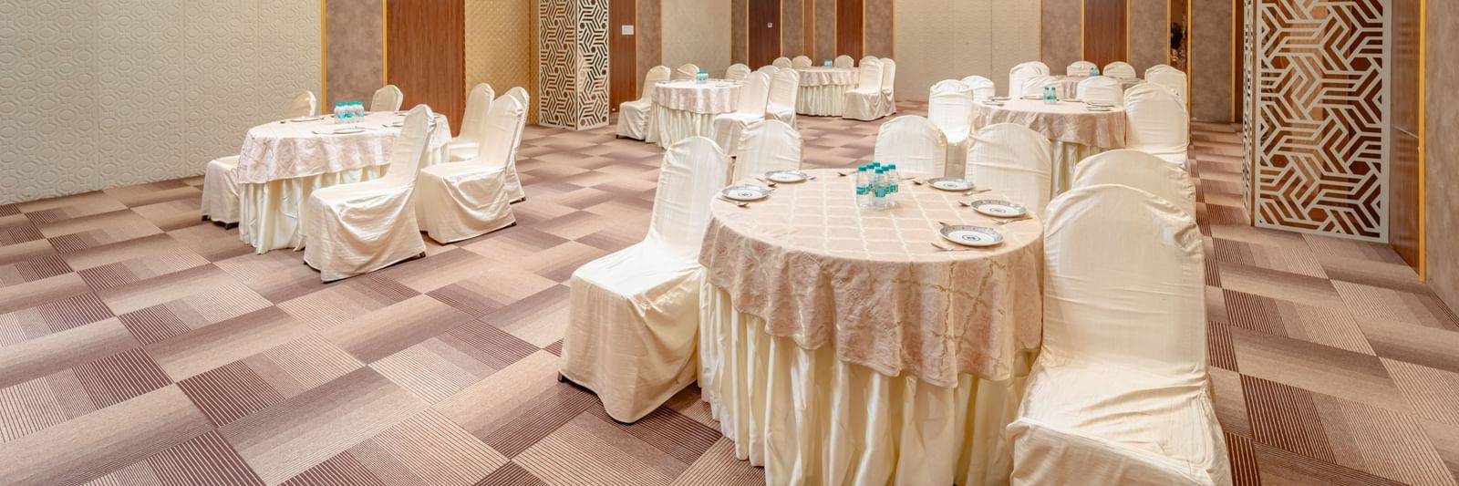 Spacious banquet hall with round tables and elegant chair covers | Meetings & Events | Pravasa Hotel, Vijayapura