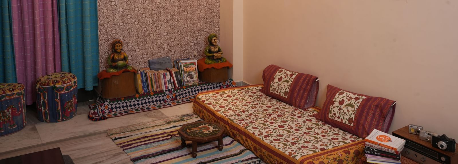 Floor-level seating with a low bed, patterned cushions, wall hanging, and decor pieces at Jaypore360 Homestay in Jaipur.