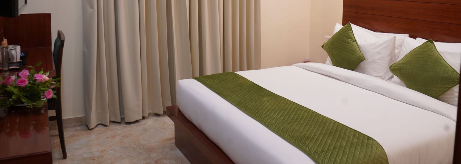 A wide shot of a hotel room bed with a white comforter and green accents.