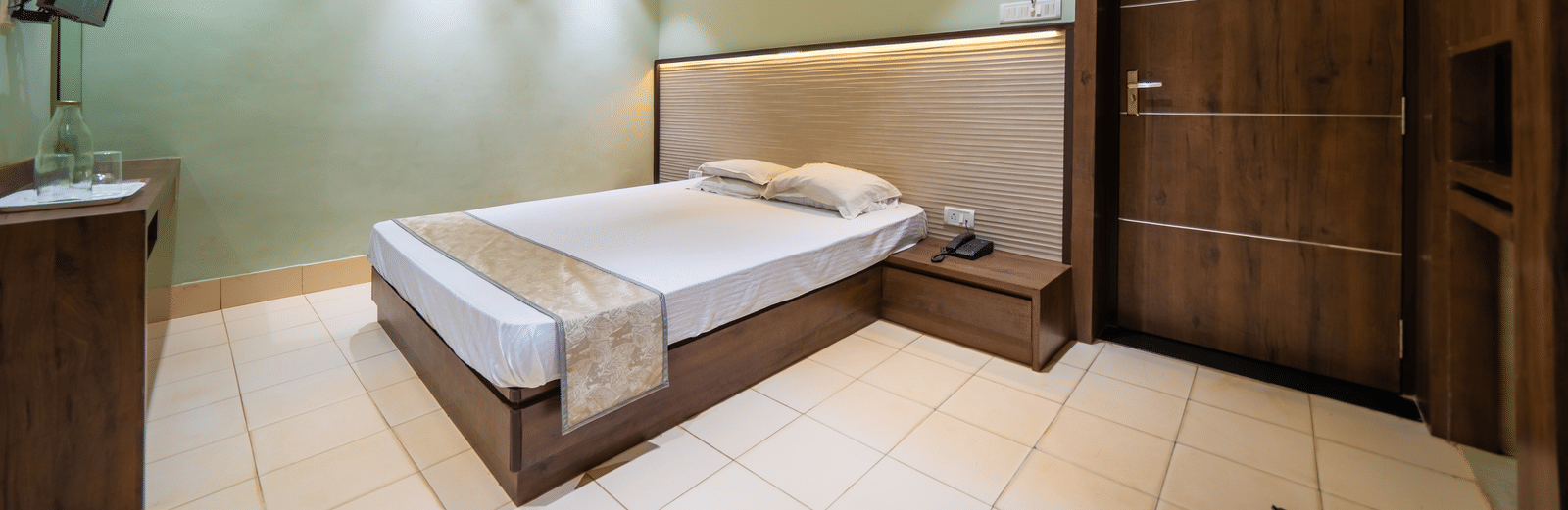 A modern hotel room with dark wood accents on the walls, a double bed, and a wall-mounted TV - Hotel Dolphin Puri