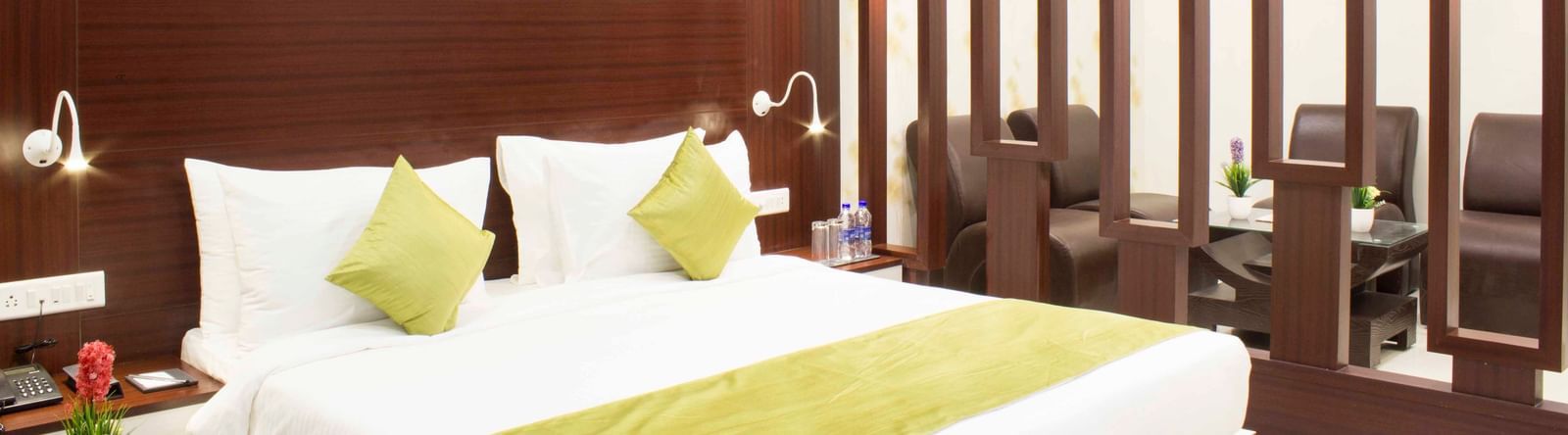 A modern hotel bedroom with a bed, green bed runner, and dark wood paneling | Daksh Suite | Daksh The Madhuvan Suites