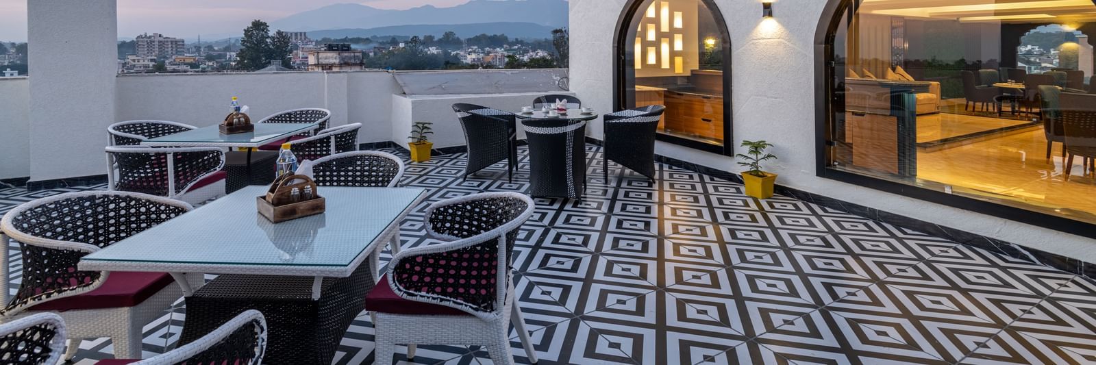 An overview of the rooftop restaurant Ruttba at DLS Grand Luxotica, Dehradun featuring dining setting on a well furnished floor with the scenic view of Dehradun city.