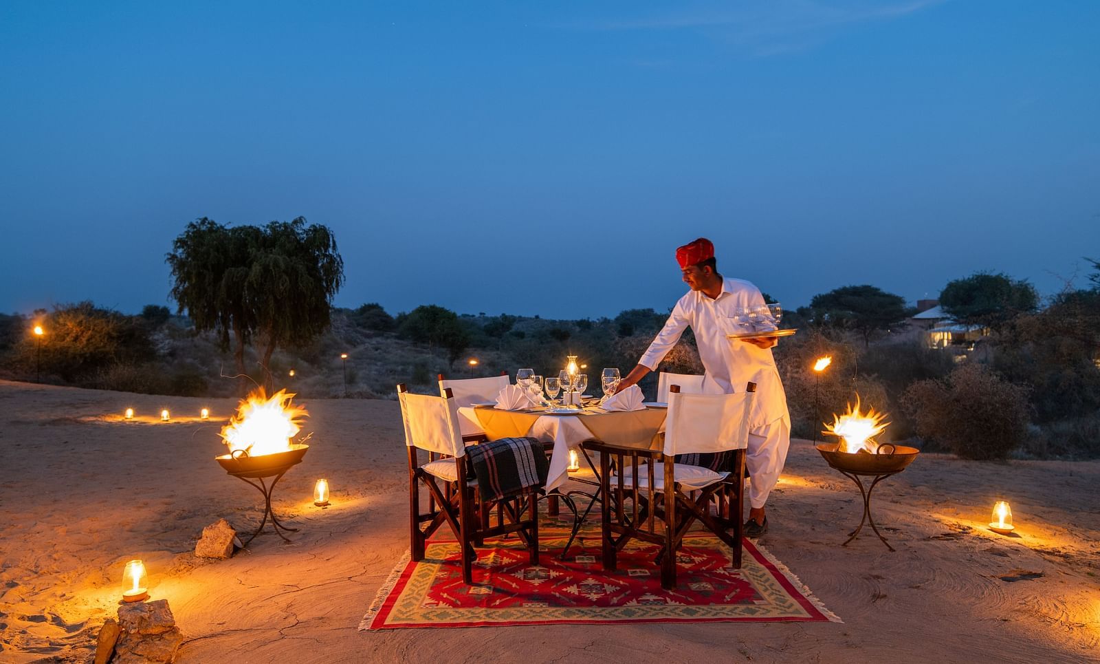 A man making an arrangement for the dinner in an outdoor setting with is decorated with lights - MANVAR Resort & Desert Camp