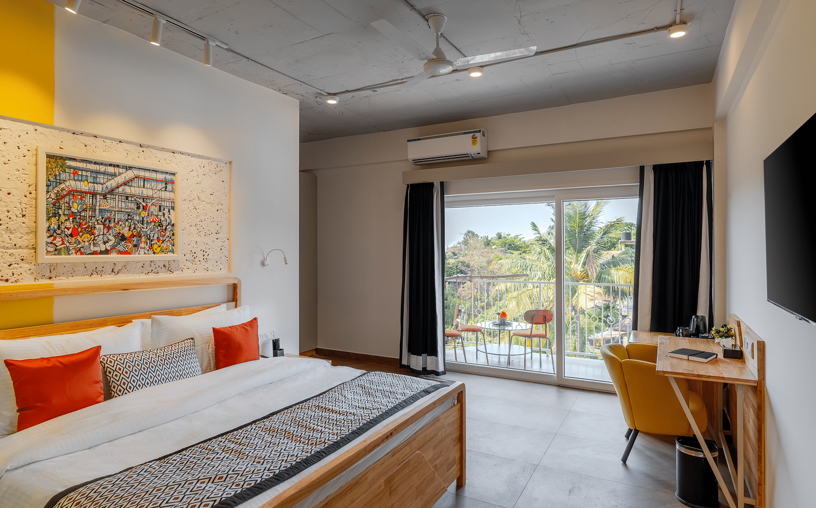 Bright hotel room with, flat TV screen, work desk and chair, vibrant art on the wall, and an access to the balcony at Bedzzz Xclusiv Morjim, Goa