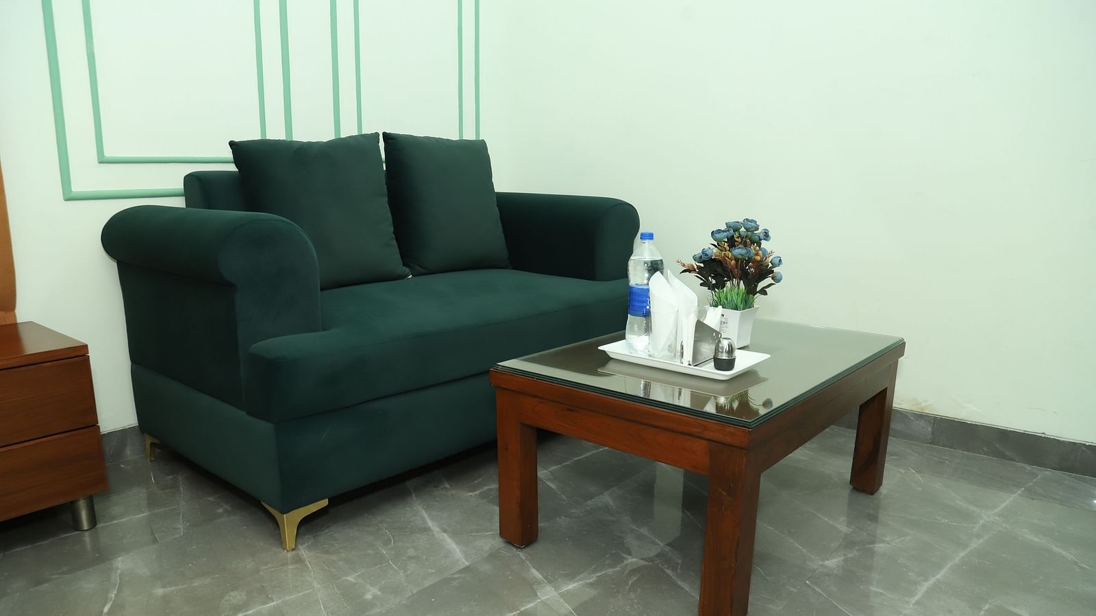 A seating area with a dark green sofa, cushions, and a small coffee table on a tiled floor - Asian Suites IFFCO Metro, Gurgaon