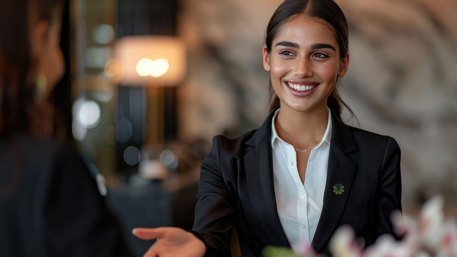 A smiling hotel receptionist welcoming a guest at the front desk.