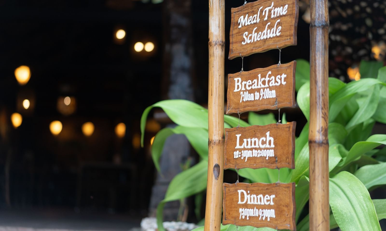 Wooden signpost at Flower Island Resort showing meal times for breakfast, lunch, and dinner along a garden path.