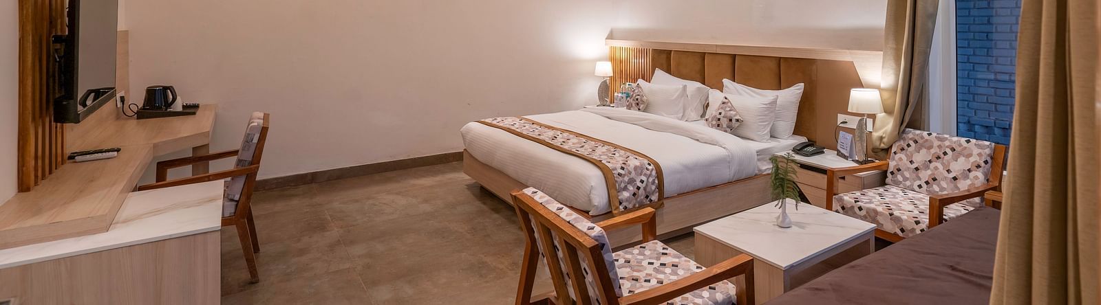 A shot of the hotel room with a king-size bed, a seating area, and a work desk.