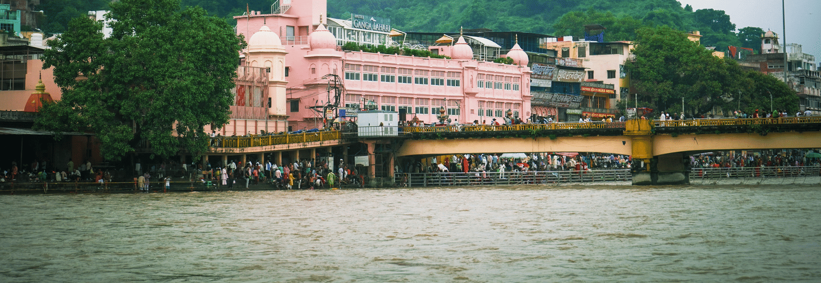  Exterior view of a river, bridge, and colourful buildings on the bank of ganges.