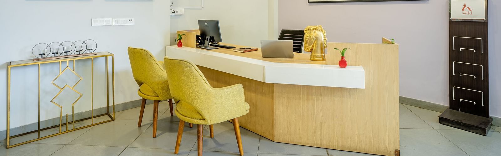 An image of a reception of the hotel where a desk and two chairs are placed | Inde Hotel Golf Course Extension