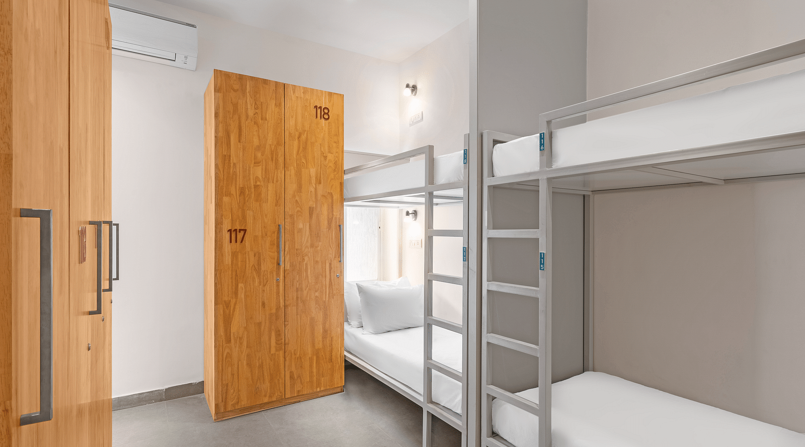 Dorms at Bedzzz in Varanasi feature a practical layout with built-in cupboards and a door, ensuring privacy and ample storage space. The design creates a comfortable environment for guests, making it an ideal choice for travelers seeking a cozy stay.