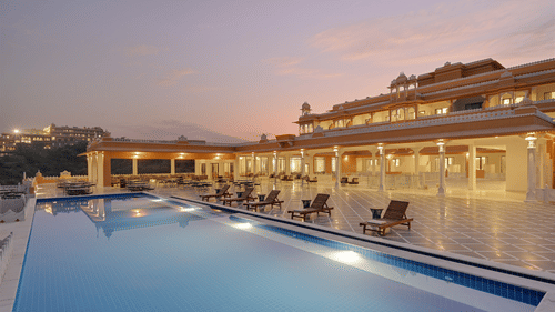 Facade of Fateh Vilas in Udaipur featuring a well lit building and a swimming pool.