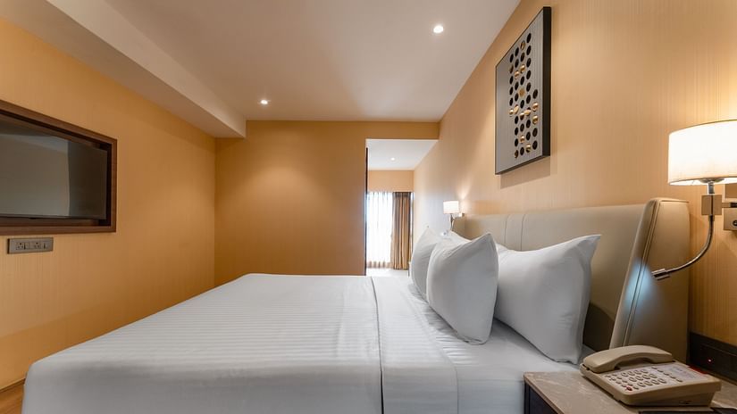  Side view of a double bed with wall-mounted TV and nightstand in a warm-lit bedroom at Clarks Inn Suites, Hyderabad